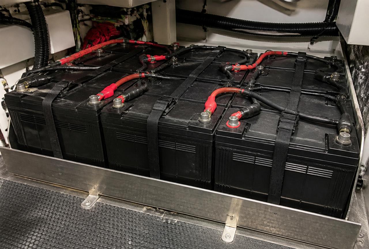 Marine battery bank strapped into a stainless tray with heavy red and black cable lugs